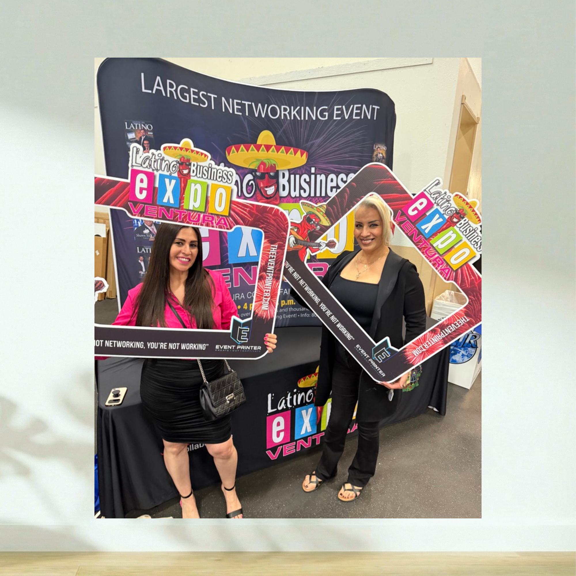 Two attendees holding a branded Latino Business Expo Ventura selfie frame