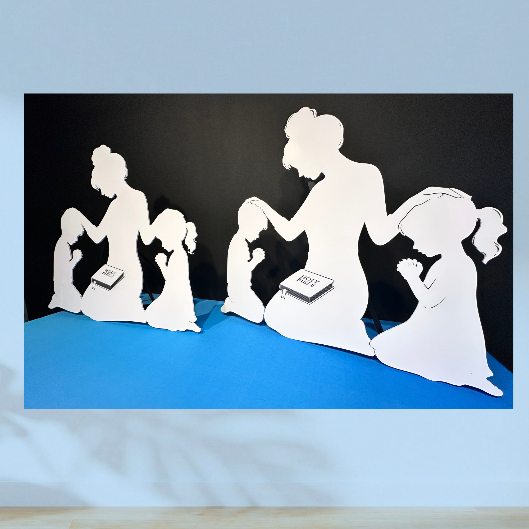 White die-cut foam board silhouettes of adults and children praying together with Bibles