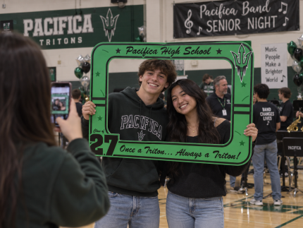 Two Pacifica High School seniors holding a custom green Tritons Class of 2027 photo frame during Band Senior Night in the school gym.